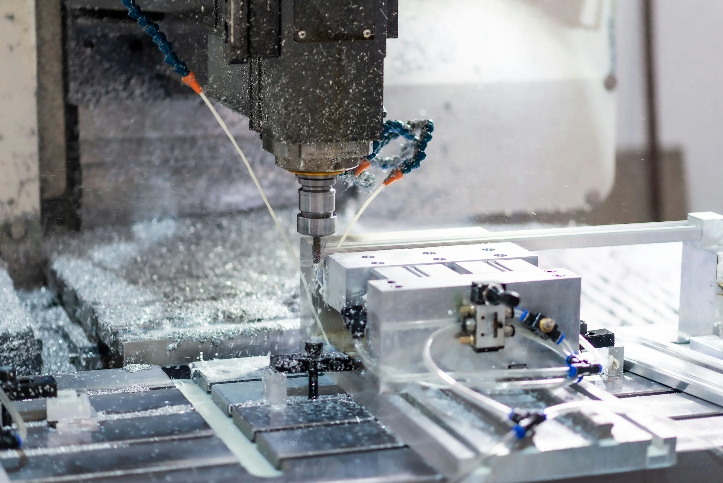 Close-up of a CNC machine machining a metal part, with coolant spray and metal shavings around.