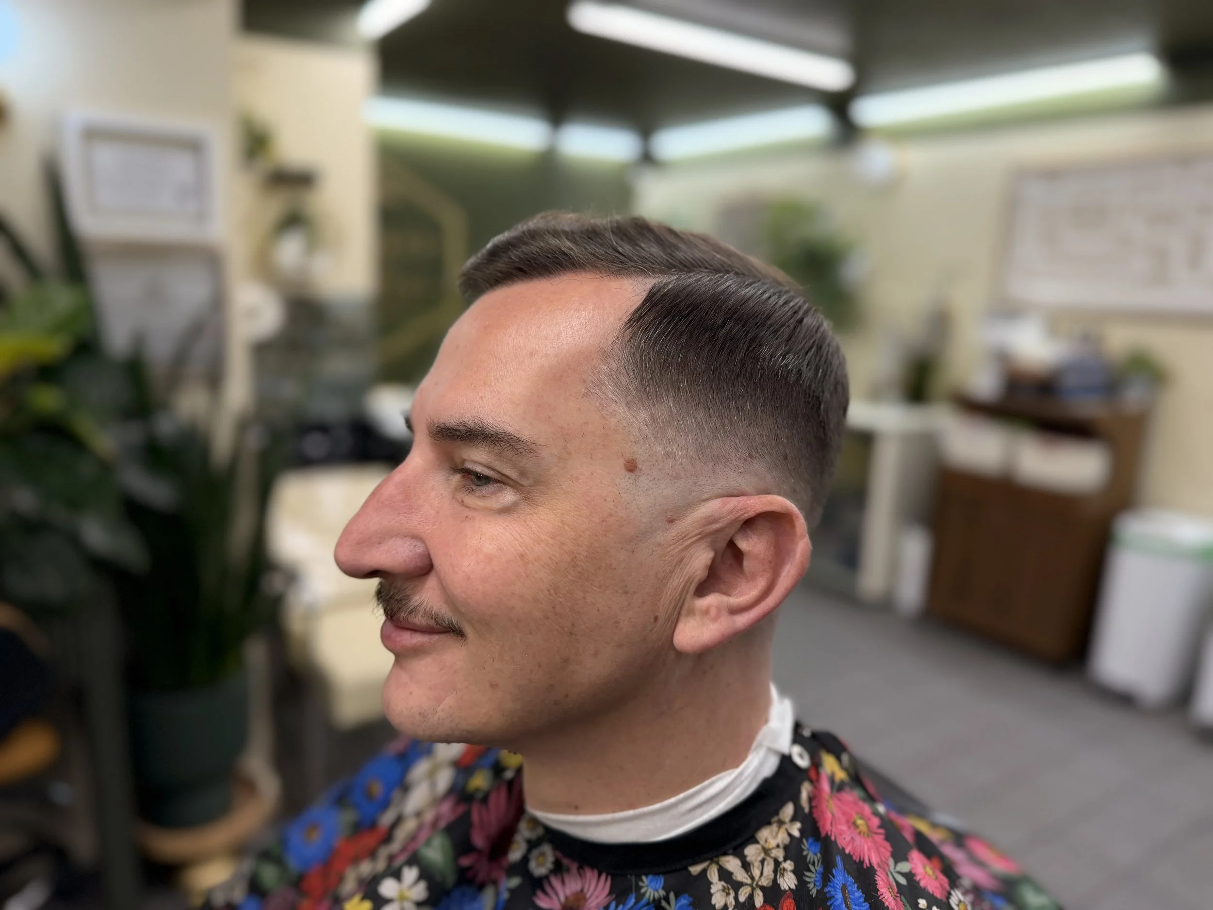 Close-up of a man with a fresh, faded haircut in a barbershop, wearing a black shirt with colorful floral pattern.