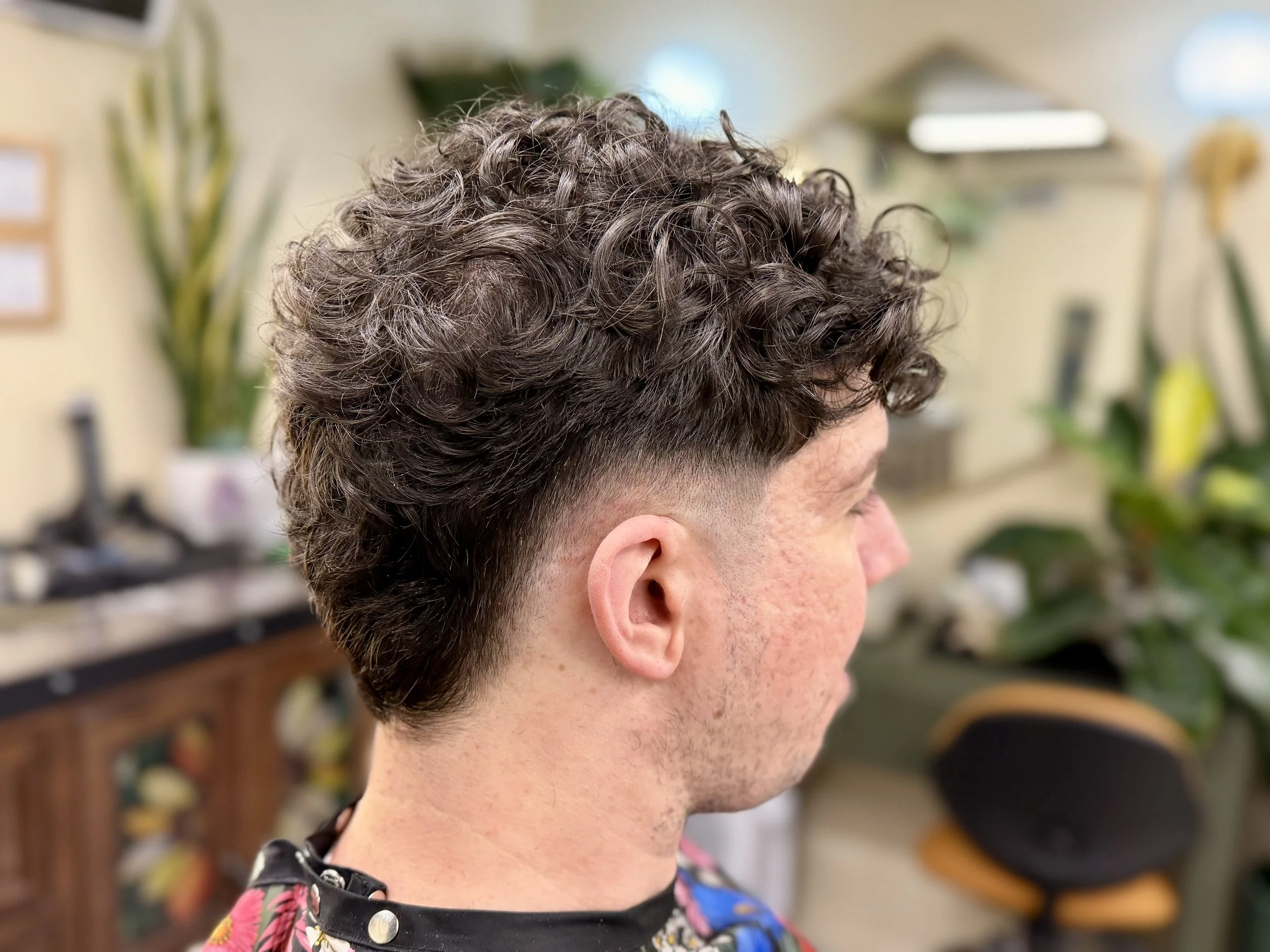 Side profile of a person with curly, short hair in a salon, wearing a colorful floral cape.