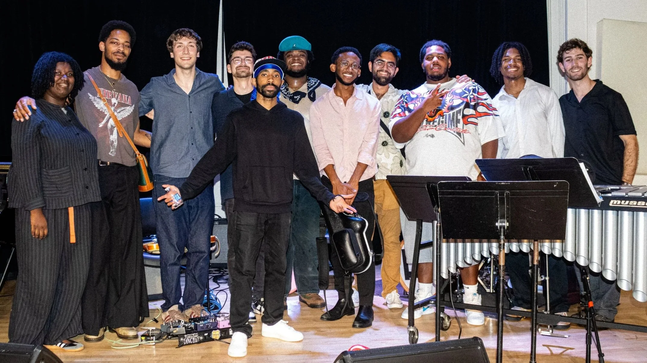 Group of people standing on stage with musical instruments and equipment, celebrating or posing for a photo.