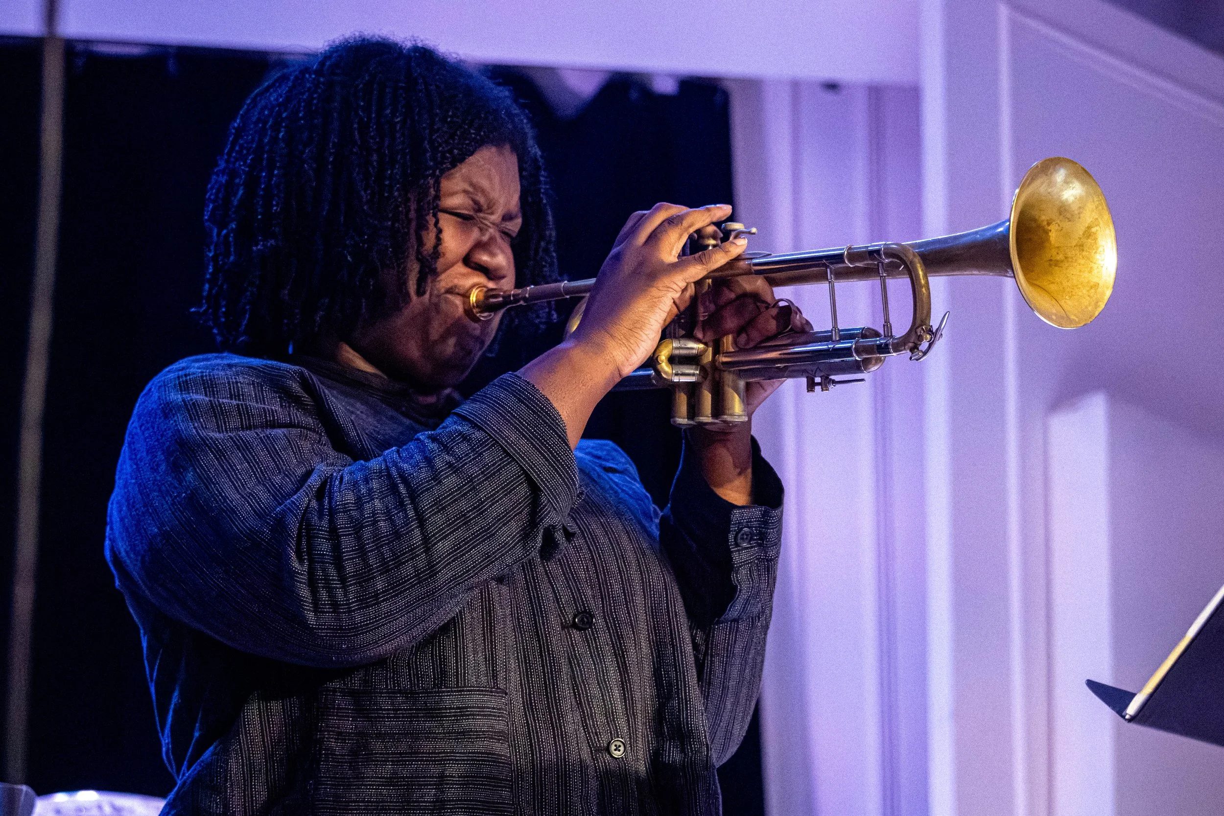 A woman with braided hair playing a trumpet.