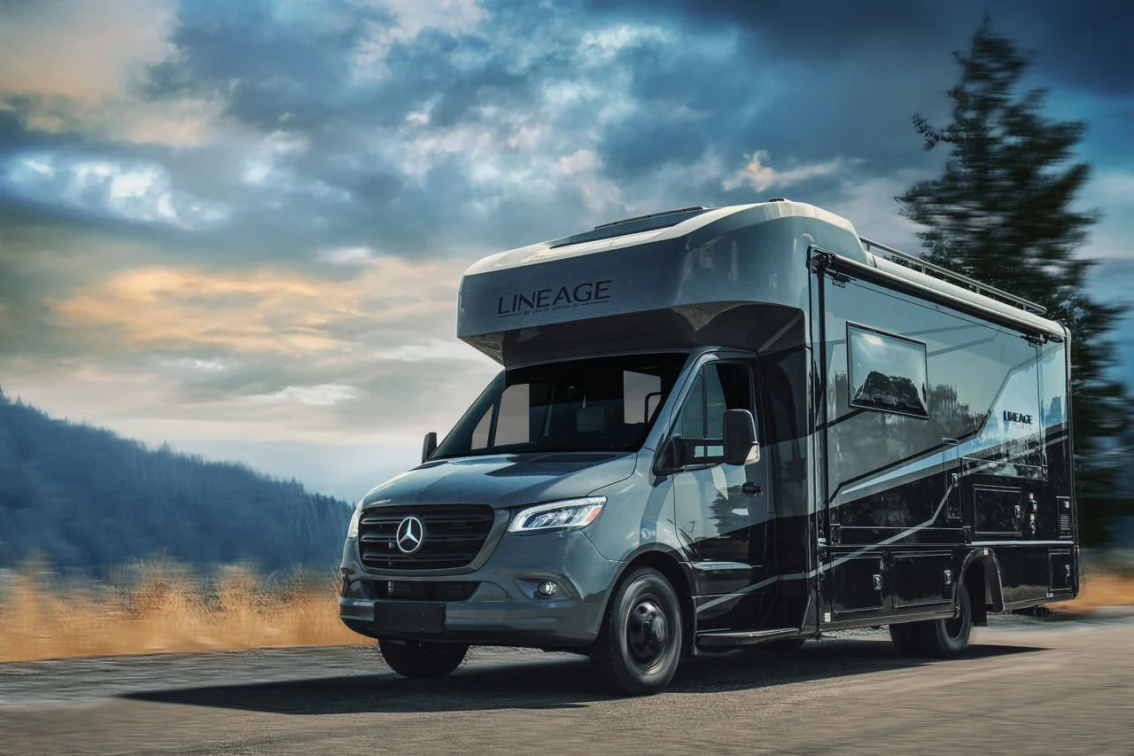 A Mercedes-Benz RV on the road with a mountain landscape and cloudy sky in the background.