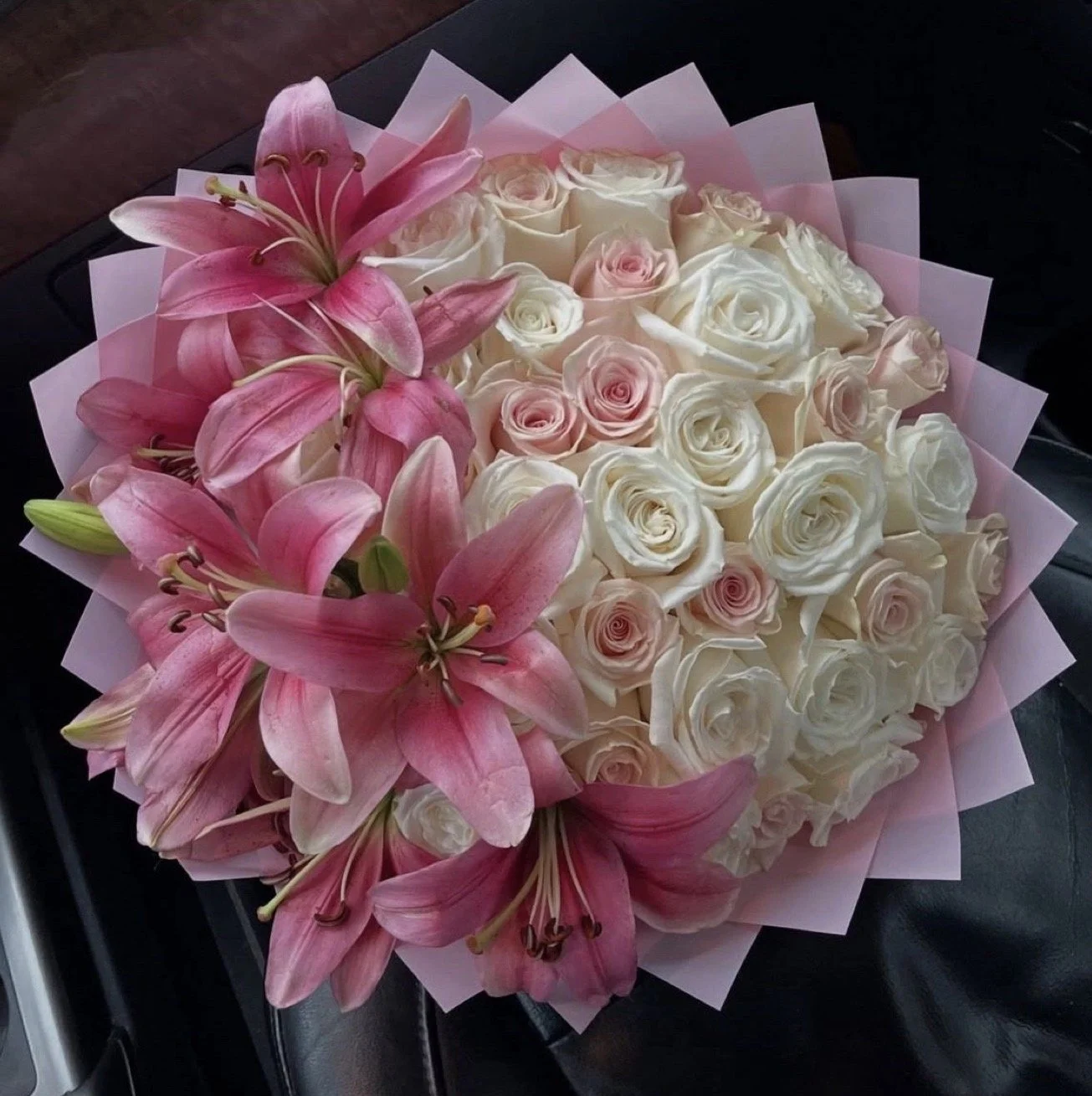 Een boeket met roze lelies en witte en roze rozen, ingepakt in roze papier.