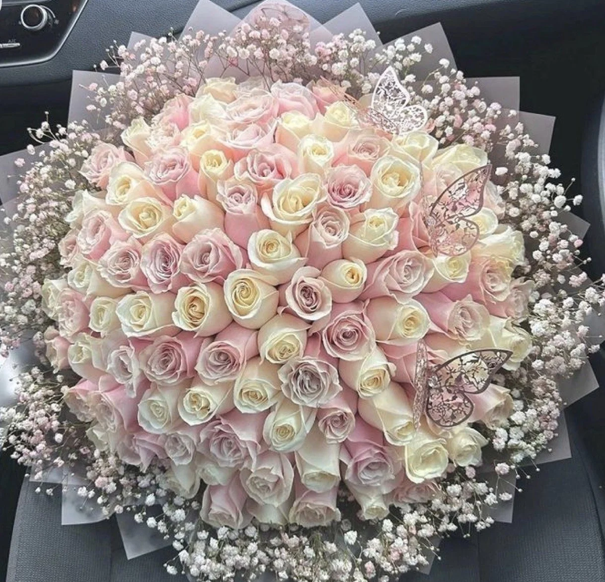 Een groot bouquet van roze en witte rozen met kleine witte bloemen en decoratieve papieren vlinders.