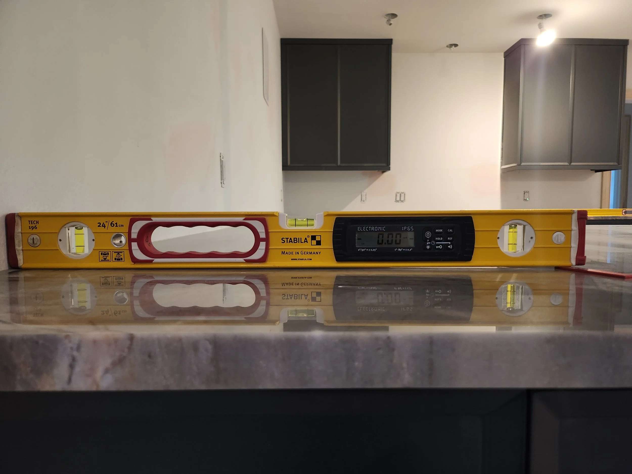 A yellow spirit level with the brand name 'Stabila' and measurements, placed on a polished surface reflecting it.