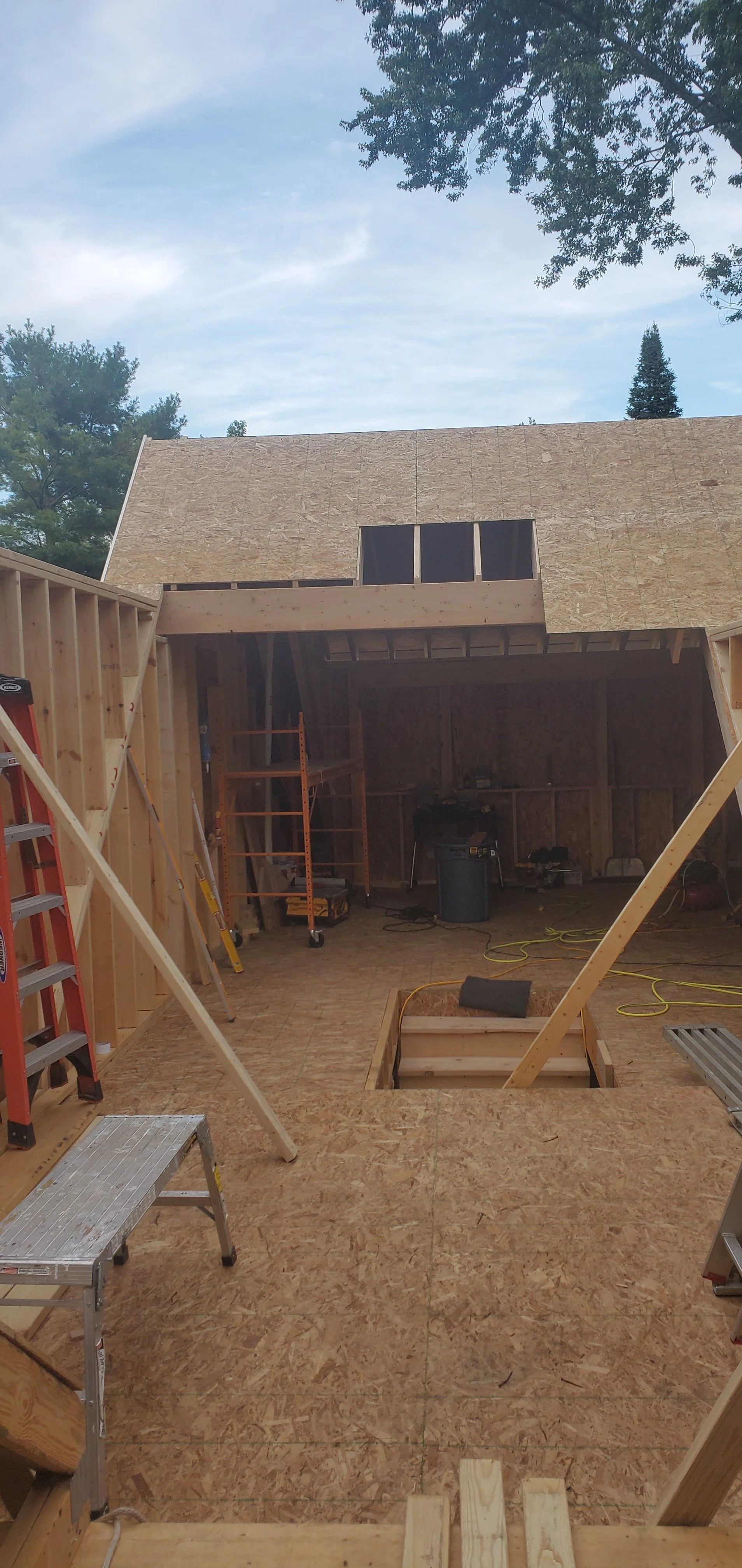 Construction site of an upstairs, with plywood walls and roof, ladders, tools, and construction equipment inside, and a stairwell.
