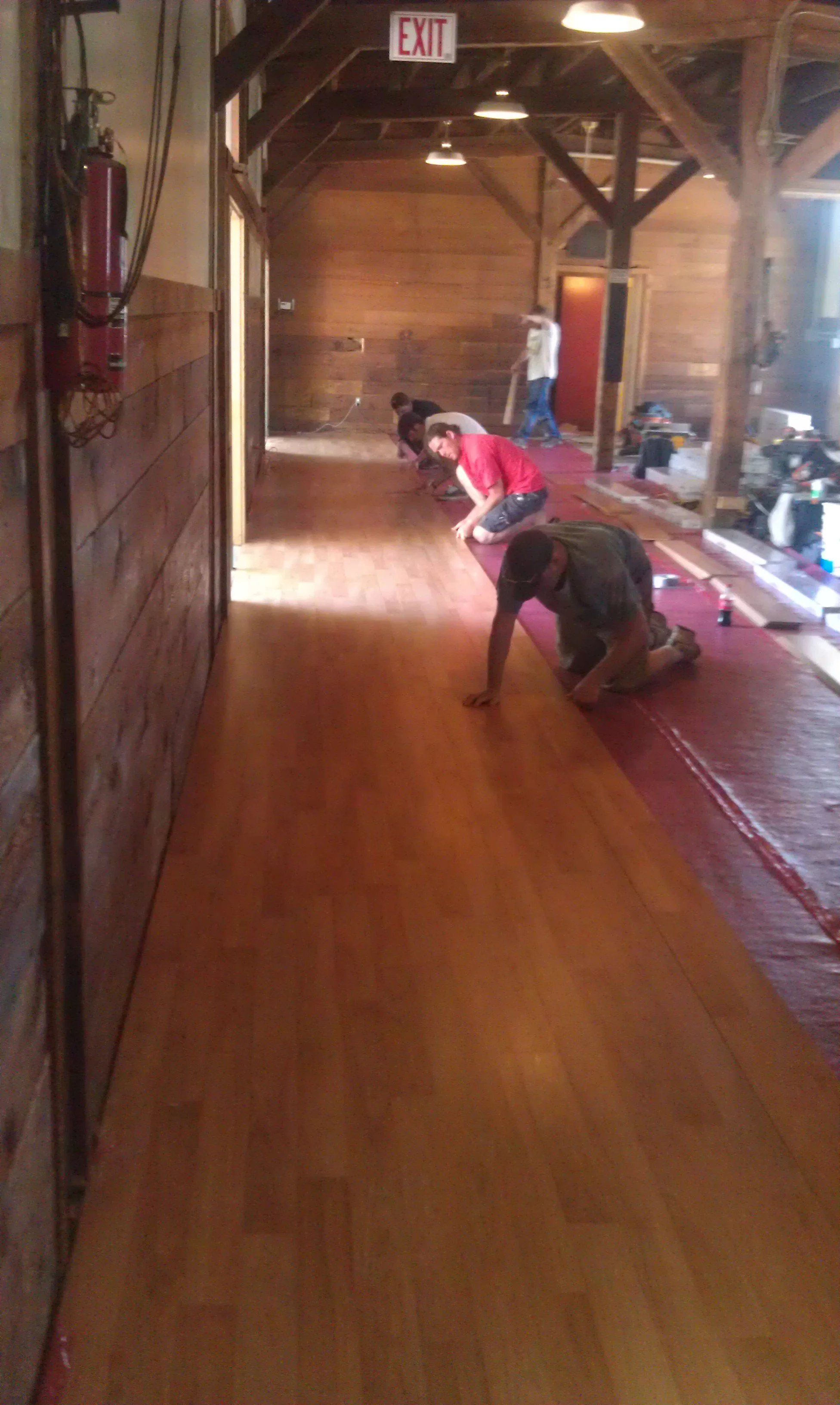 People installing a wood floor in a rustic wooden building with wooden beams, tools and materials scattered on the floor.