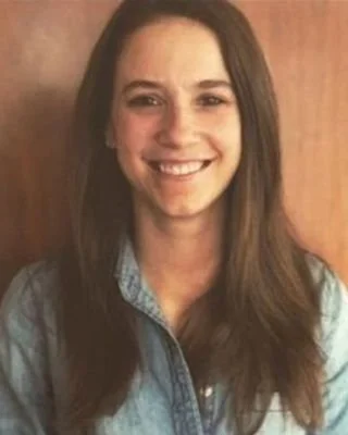 A woman with long brown hair wearing a denim jacket, smiling at the camera.