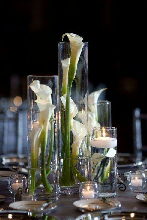 Vase centerpiece with white calla lilies and green stems, surrounded by candles on a dark table setting.