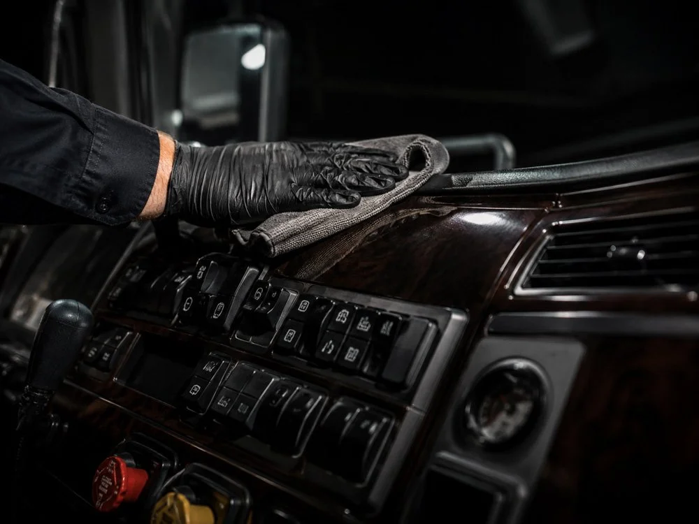 Person wearing black gloves cleaning the dashboard of a vehicle with a cloth.