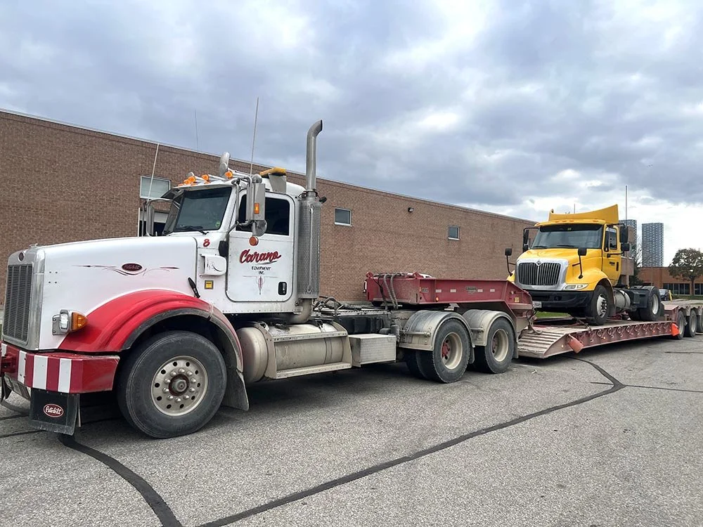 A semi-truck with a red and white cab and a yellow semi-truck trailer carrying a yellow truck.