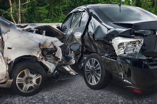 A front-end collision between two cars on a gravel road, with significant damage to both vehicles' fronts.