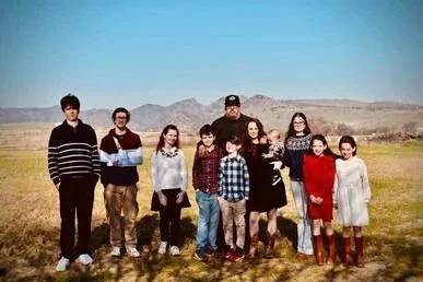 Group of ten people standing outdoors in a field with mountains in the background.