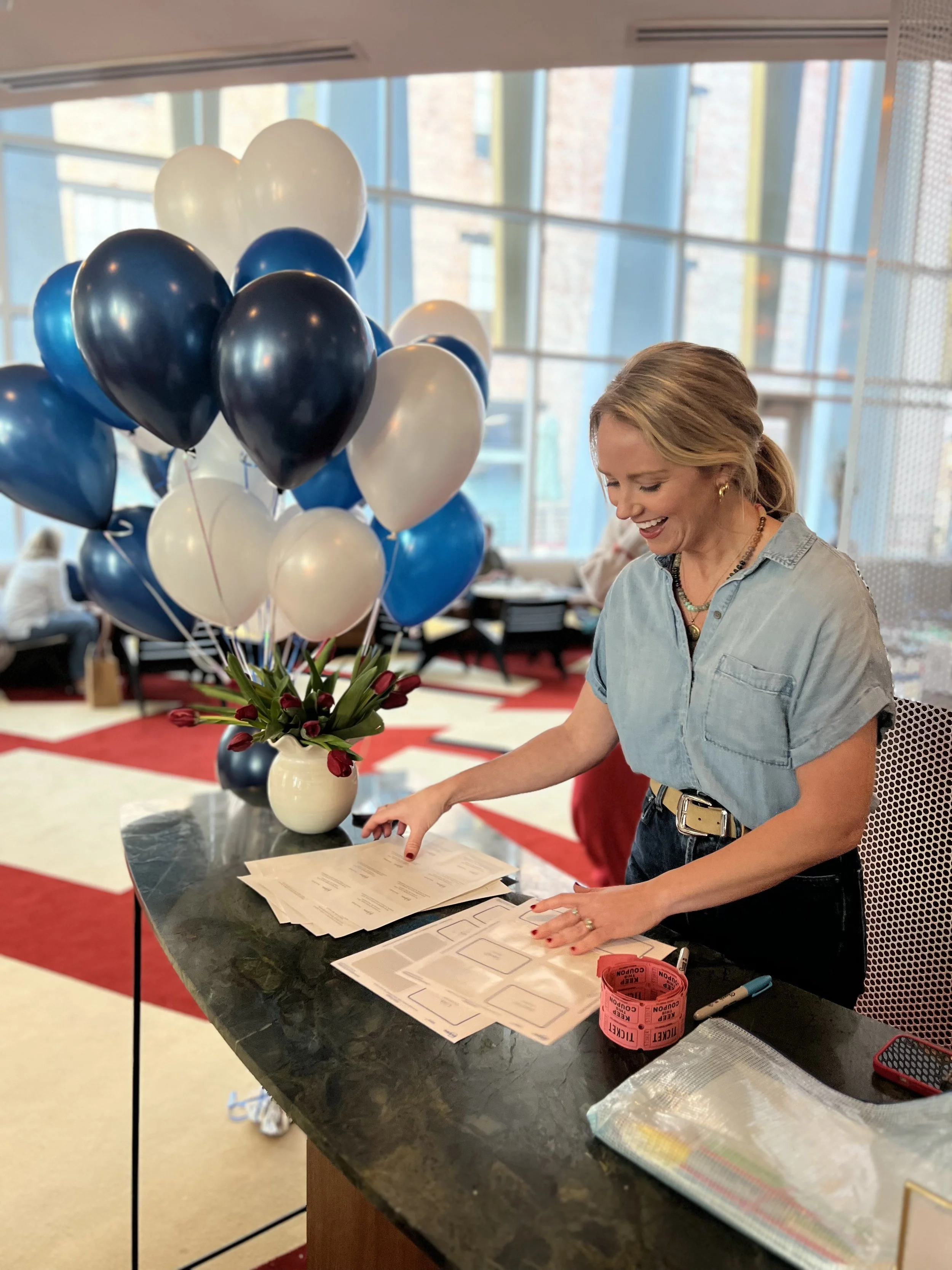 A woman with blonde hair smiling and pointing at mahjong papers.