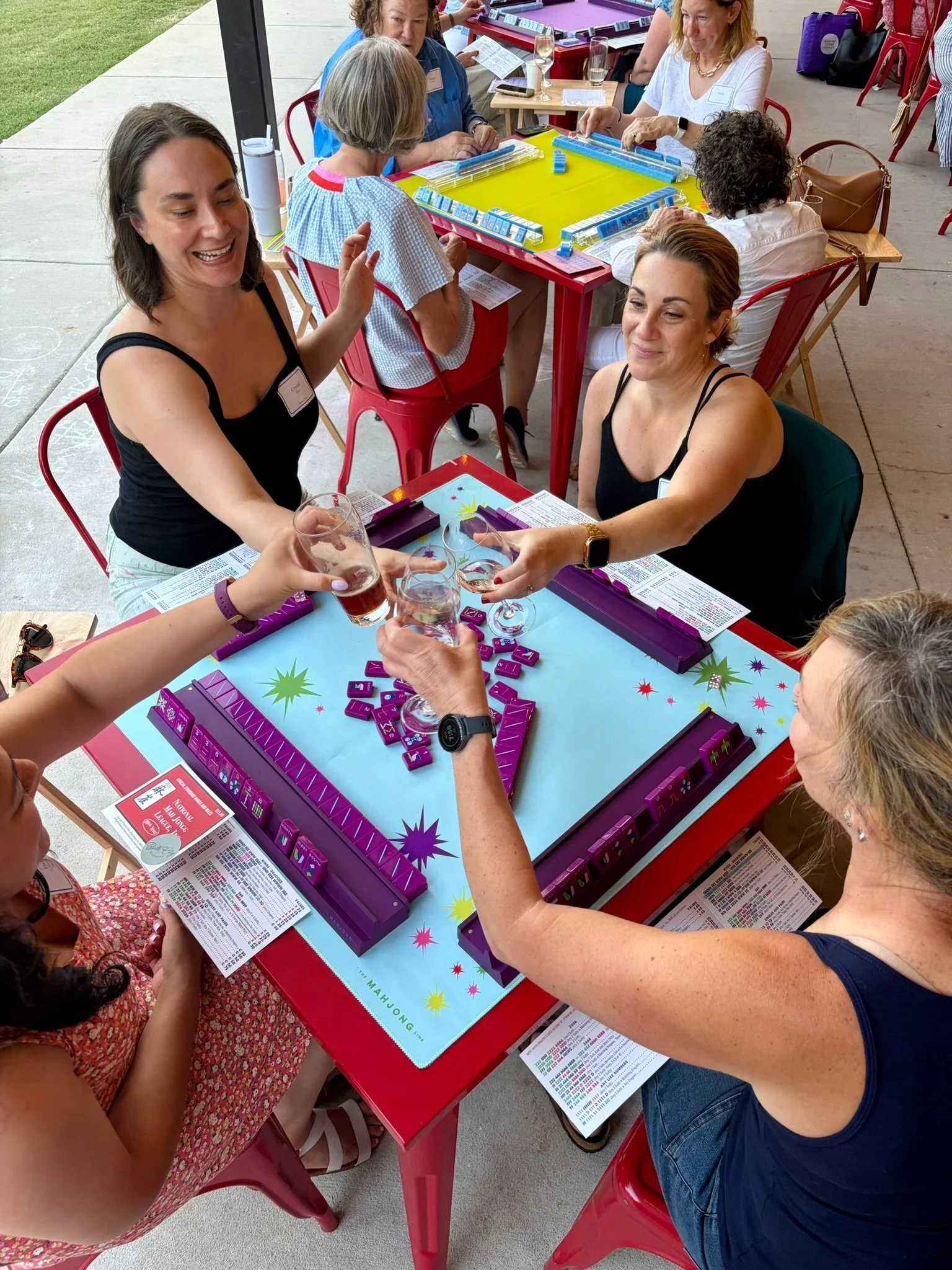 People playing a group Mahjong game at a social gathering, with drinks on the table.