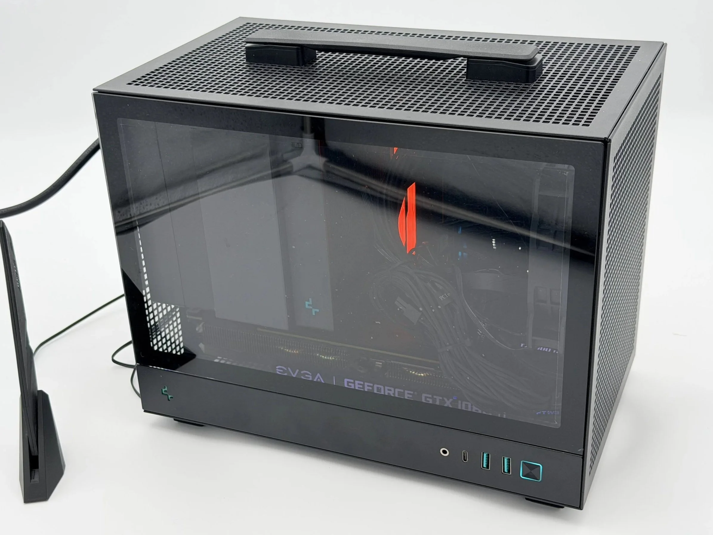A black computer case with a transparent side panel, showing internal components with red and blue lighting, and branded EVGA GeForce GTX 10 graphics card, placed on a table with a black stand.