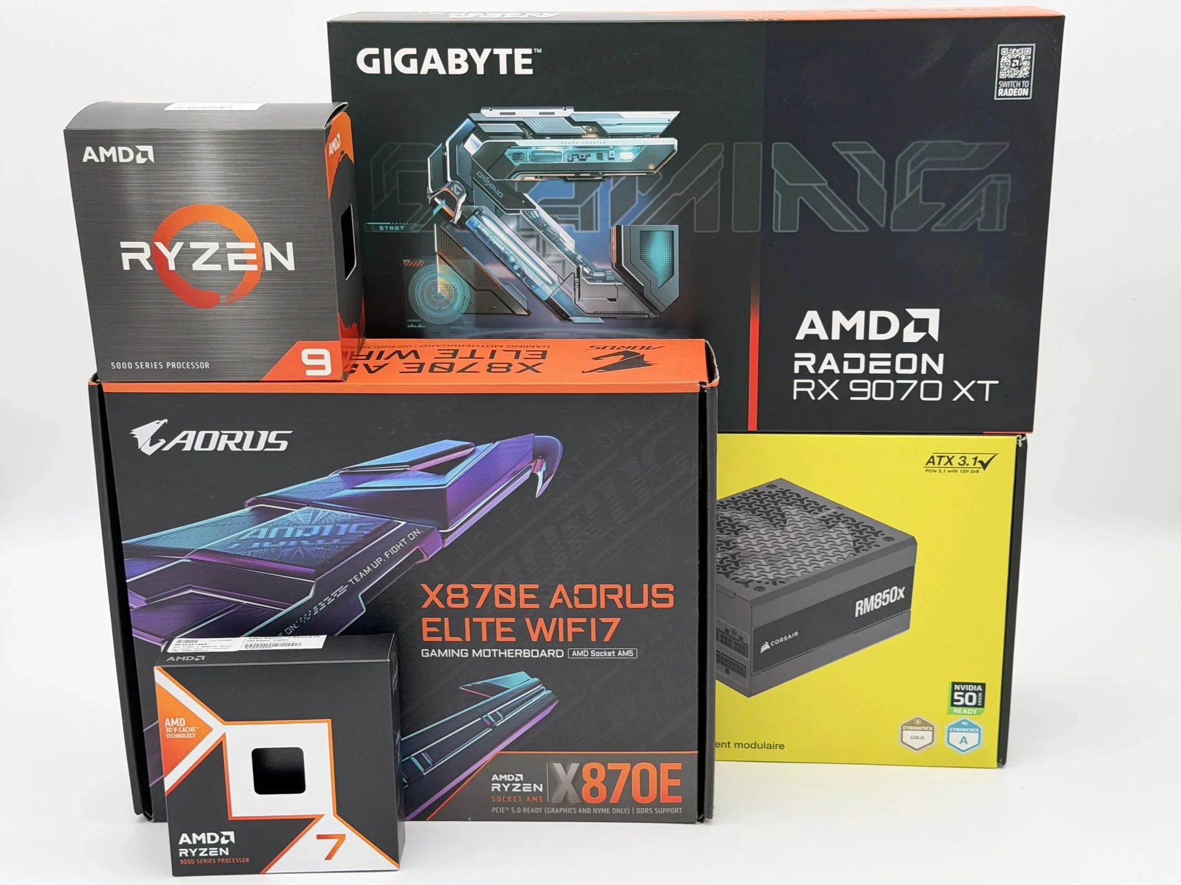 Boxes of computer hardware components, including a GIGABYTE AMD Ryzen 9 processor, a GIGABYTE AMD Ryzen X870E Elite WiFi 7 motherboard, an ASUS AORUS graphics card, and a Corsair RM850x power supply.