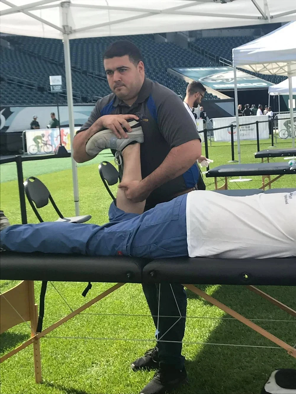 A man is receiving a massage on his leg from a professional in an outdoor setting, possibly at a sports event or medical tent.