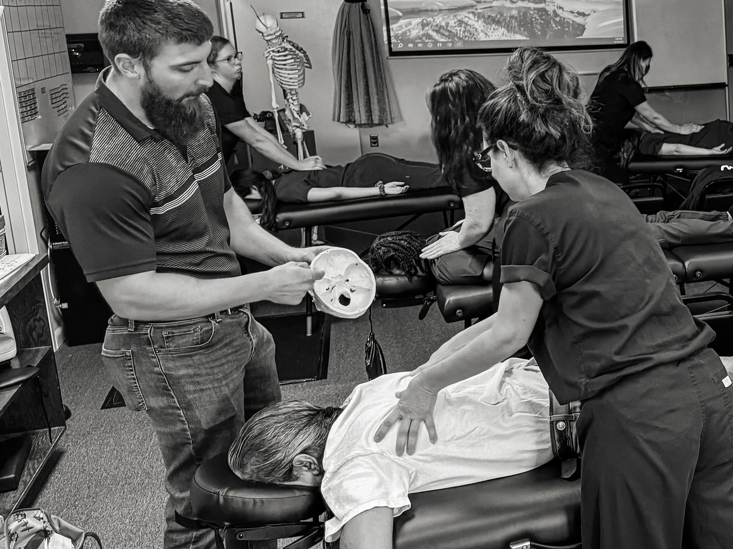 A group of people providing CPR to a person lying on a hospital bed in a medical training room.