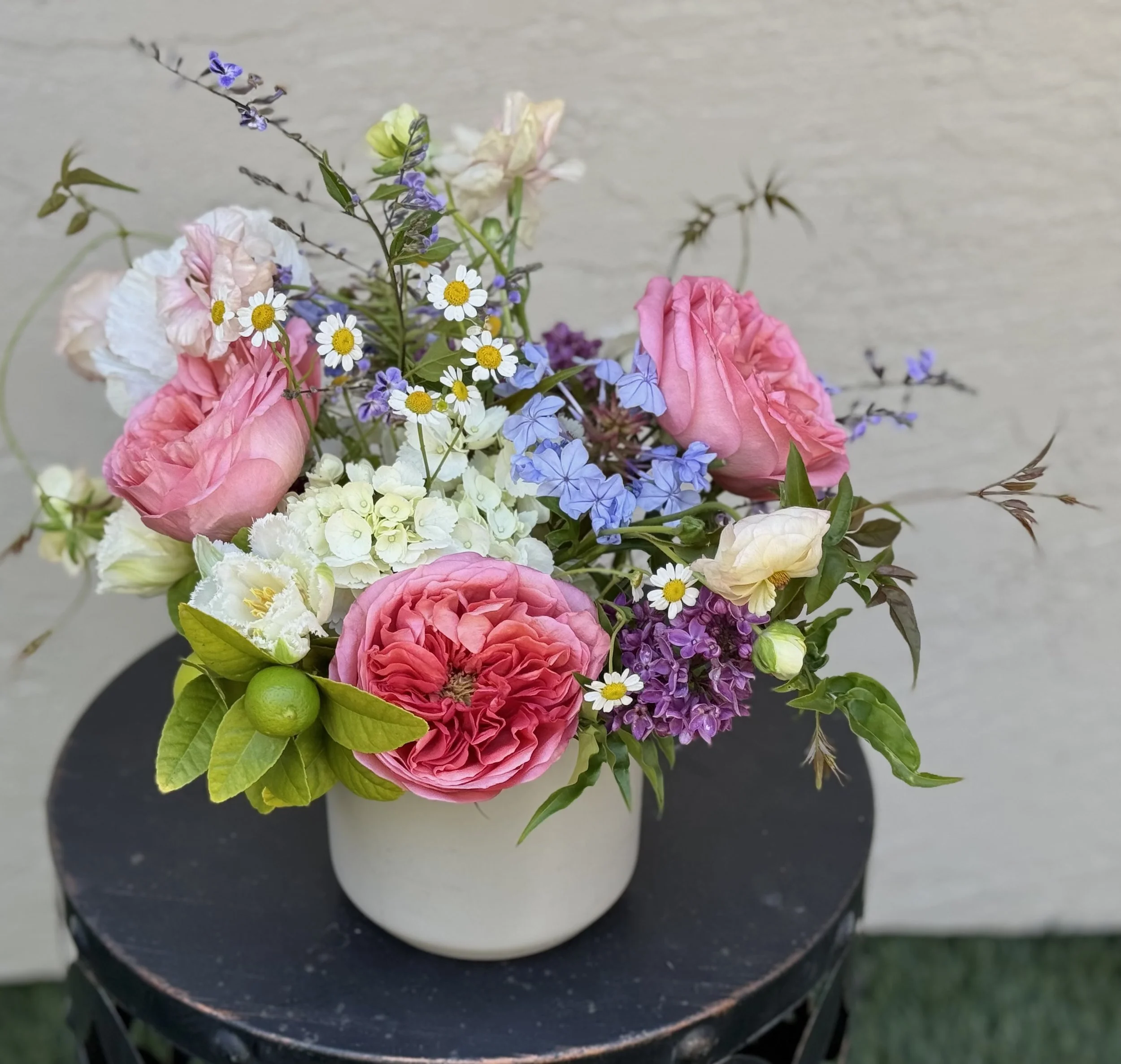 Top view of a bouquet of pink, white, purple, and yellow flowers with green leaves, placed on a black round surface.