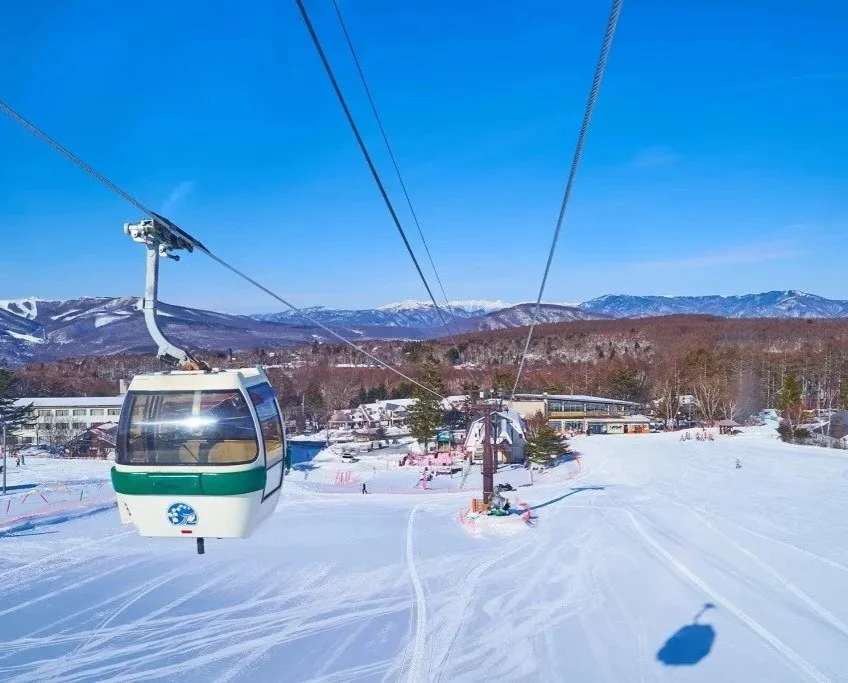 Ski gondola with snow-covered ground and mountains in the background on a clear, sunny day.