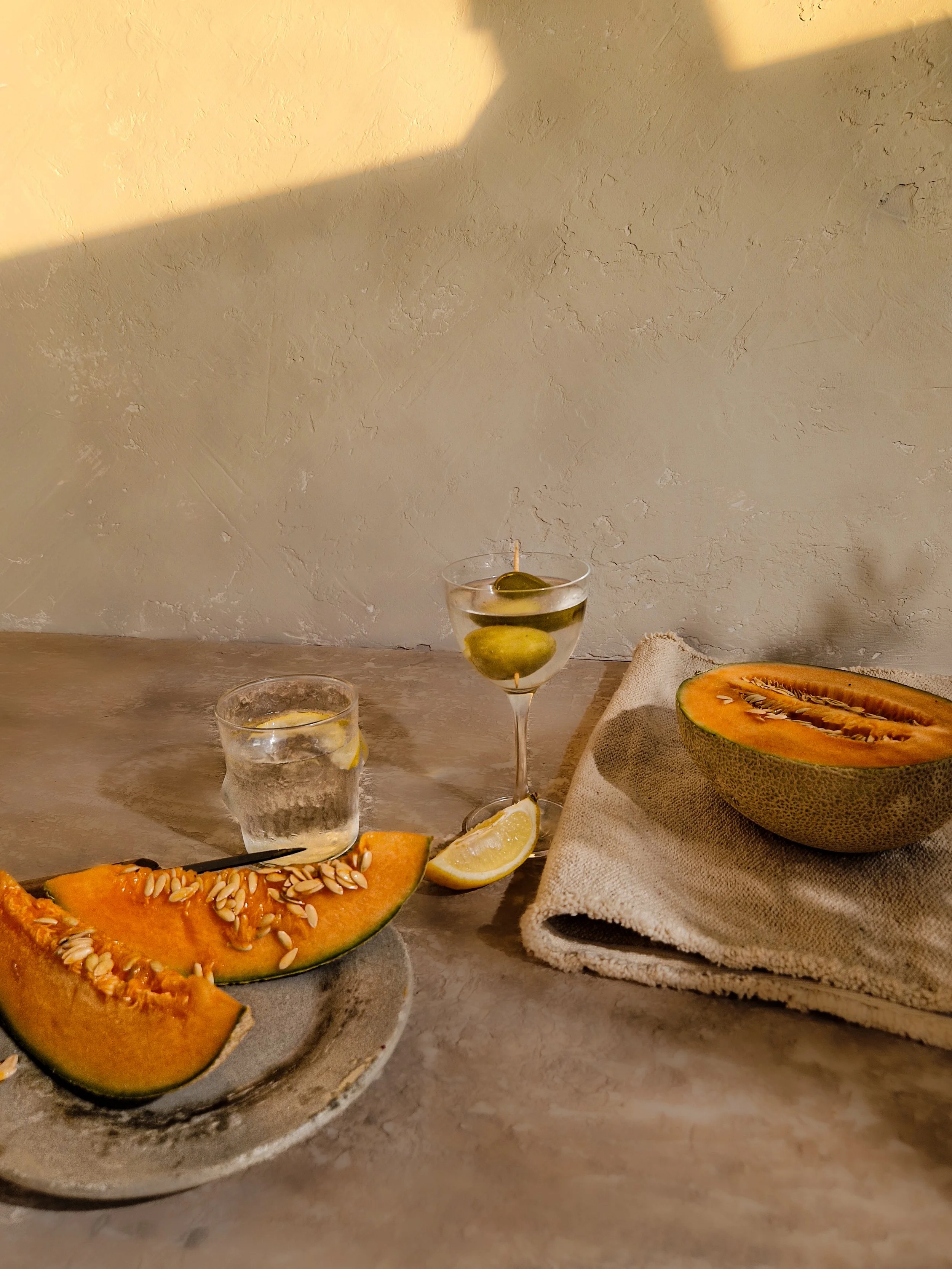 Editorial still life photography featuring sliced melon, artisanal glassware, and a draped linen cloth bathed in warm, directional sunlight. Shot by Franziska Studio, an editorial product photographer and creative director in London.