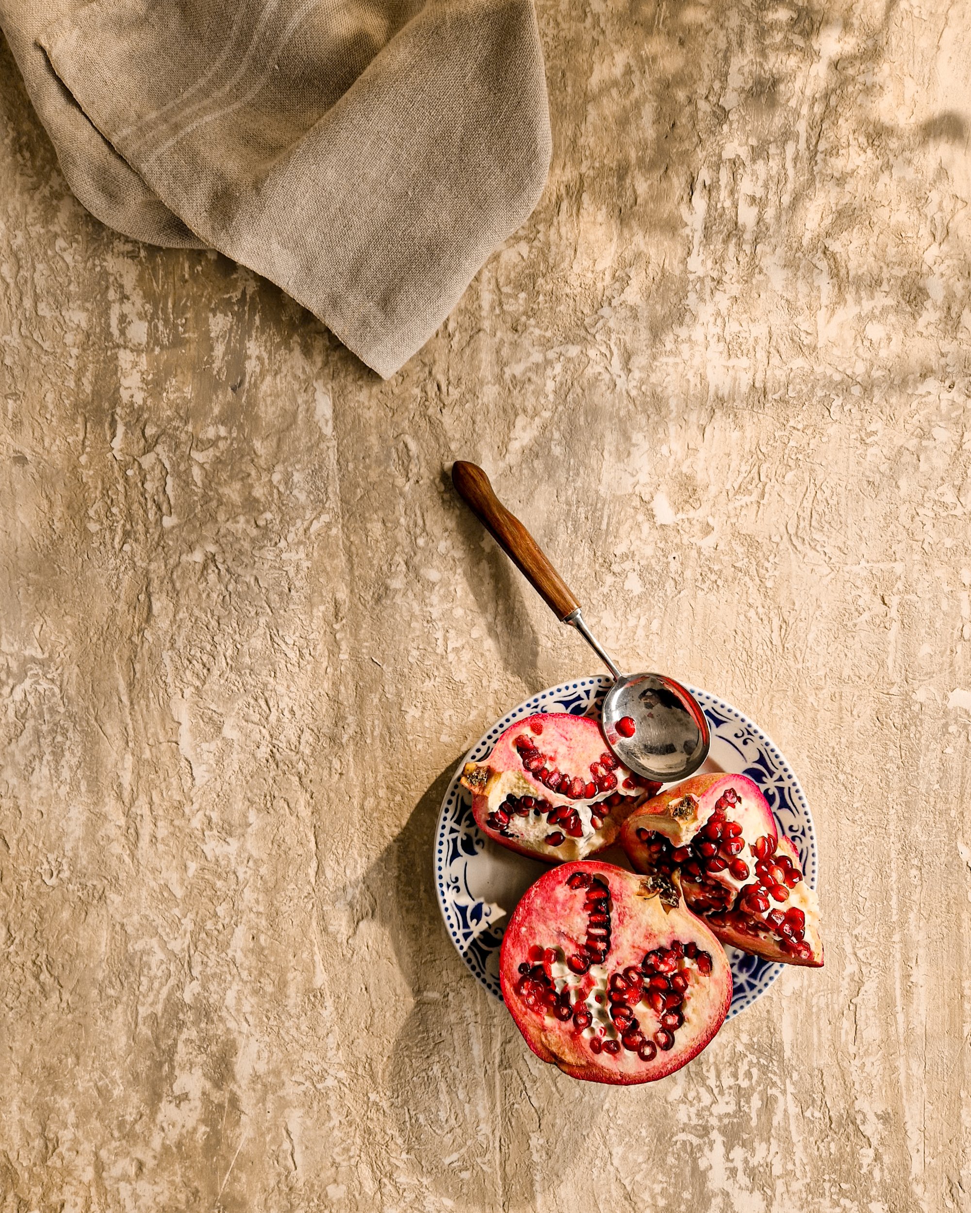 Close-up tactile detail of a folded linen napkin on a textured plaster surface with dappled sunlight and deep shadows. High-end editorial product photography in London by Franziska Studio.