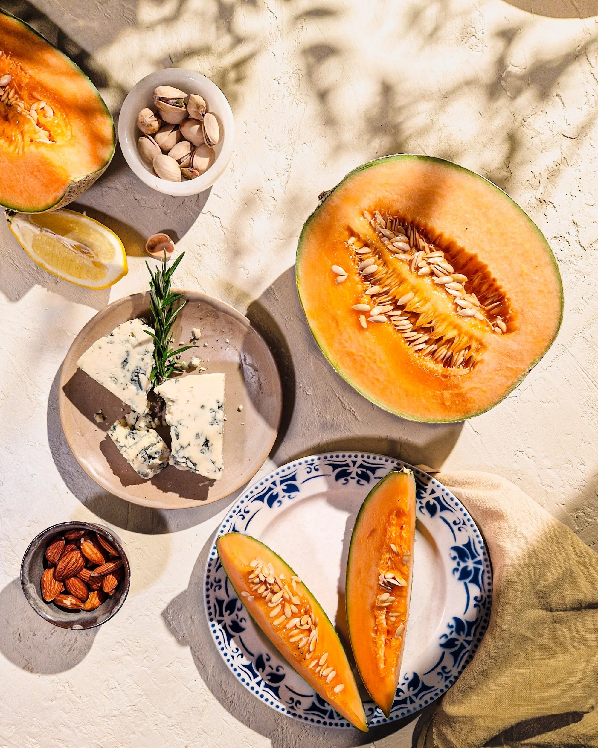 Overhead editorial food styling and commercial photography featuring sliced melon, a bowl of pistachios, and fresh citrus. Sun-drenched Mediterranean aesthetic by London still life photographer Franziska Studio.
