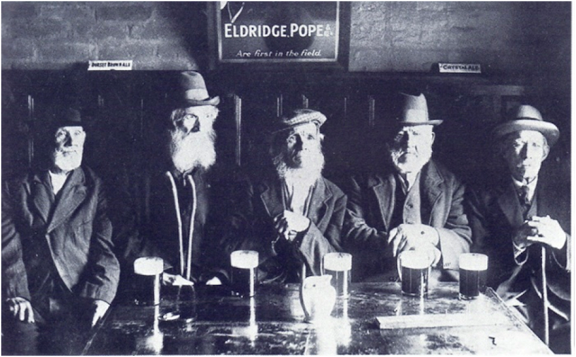 Black and white photograph of five men sitting at a bar, each with a glass of beer in front of them. The men are dressed in suits and hats, with beards and mustaches. A sign with the text 'ELDRIDGE POPE' and 'Are First in the Field' is visible in the background.