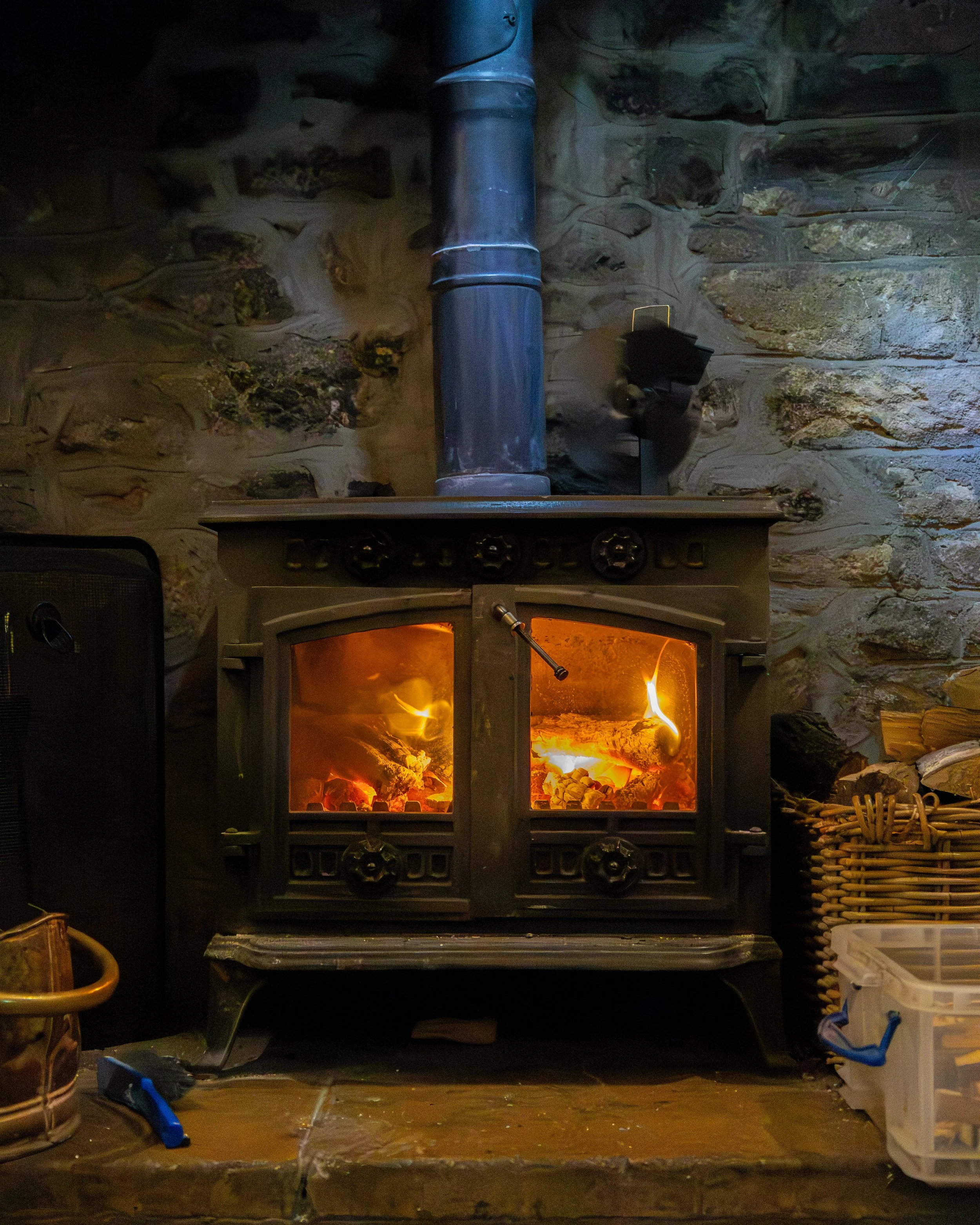 A fireplace with a burning fire, a metal stove pipe above it, and a brick wall behind it. 