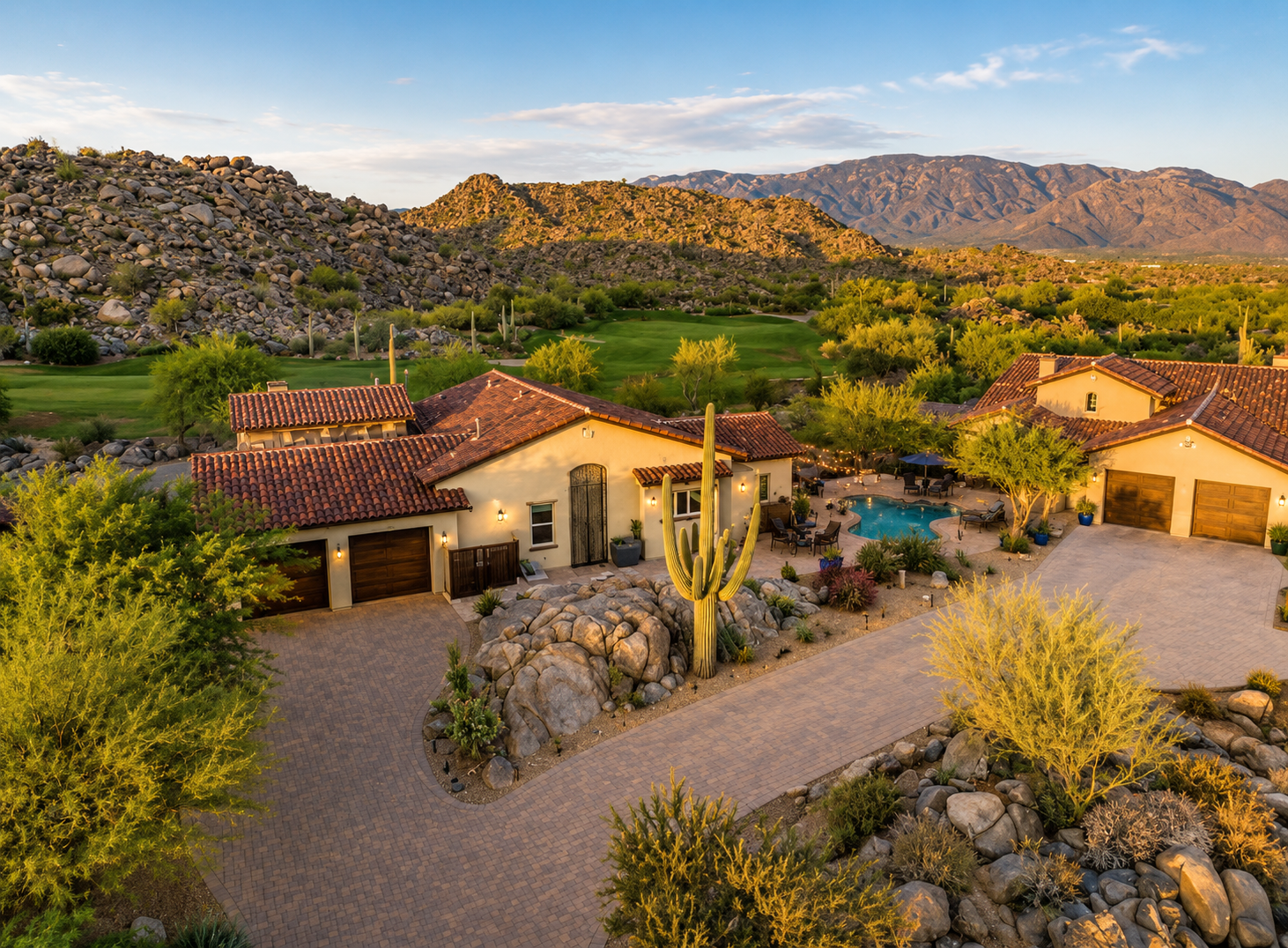 A luxurious house with Spanish-style architecture, a red tiled roof, a swimming pool, and desert landscaping with cacti and rocks, set in a desert landscape with mountains in the background.
