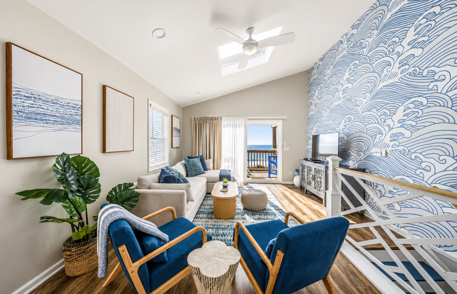 Living room with ocean view, blue and white decor, sky visible from balcony, ceiling fan, artwork, plants, and seating area with sofa and armchairs.