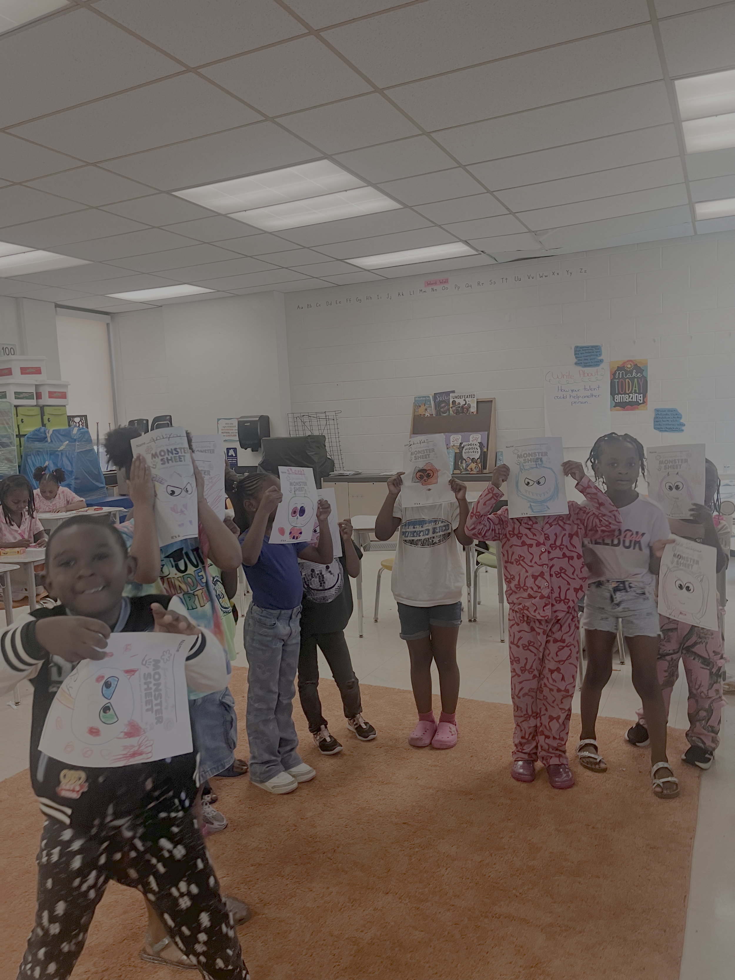 A group of children in a classroom holding up drawings of monster faces.