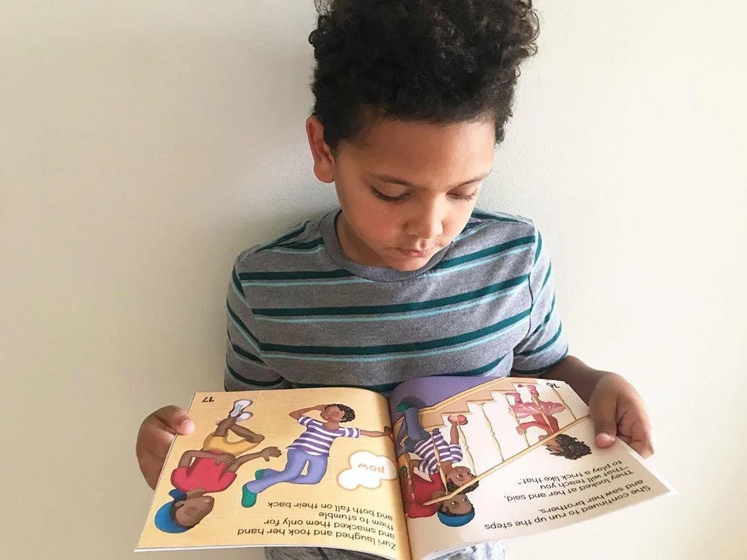 Young boy reading a colorful children's picture book with illustrations of children and a speech bubble.