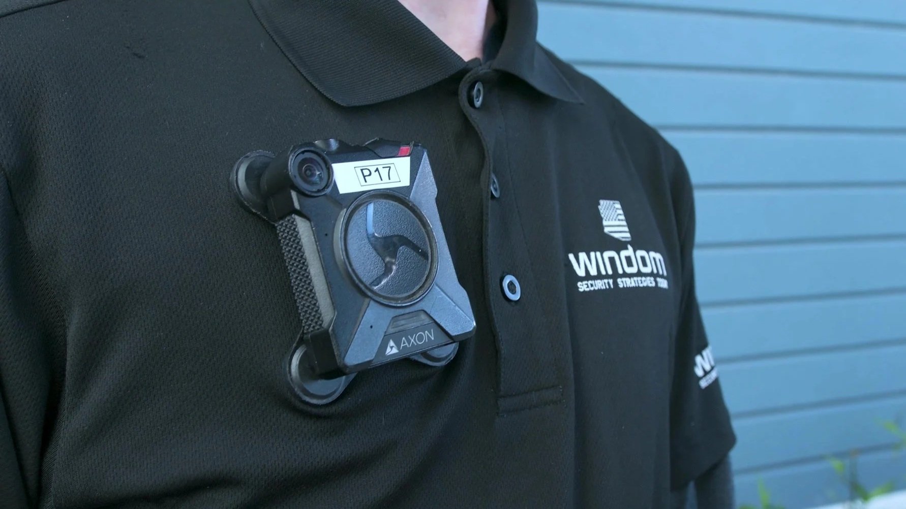 Close-up of a security officer wearing a black uniform with an Axon taser holstered on the chest, and a patch on the shirt that reads 'WINDOM Security Strategies'.