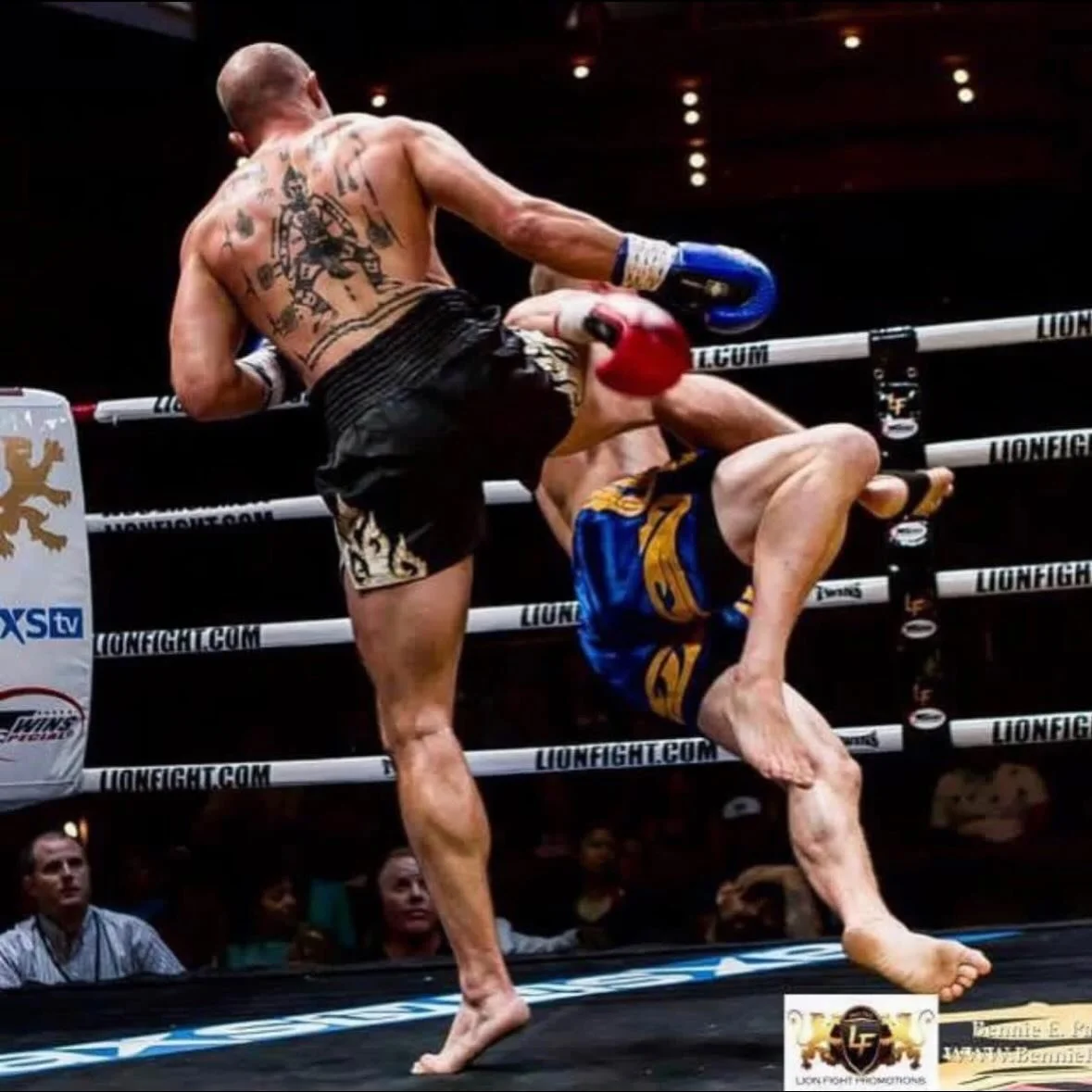 Two mixed martial arts fighters engaged in a fight inside a boxing ring, with one fighter delivering a kick to the other, who is in a defensive position.