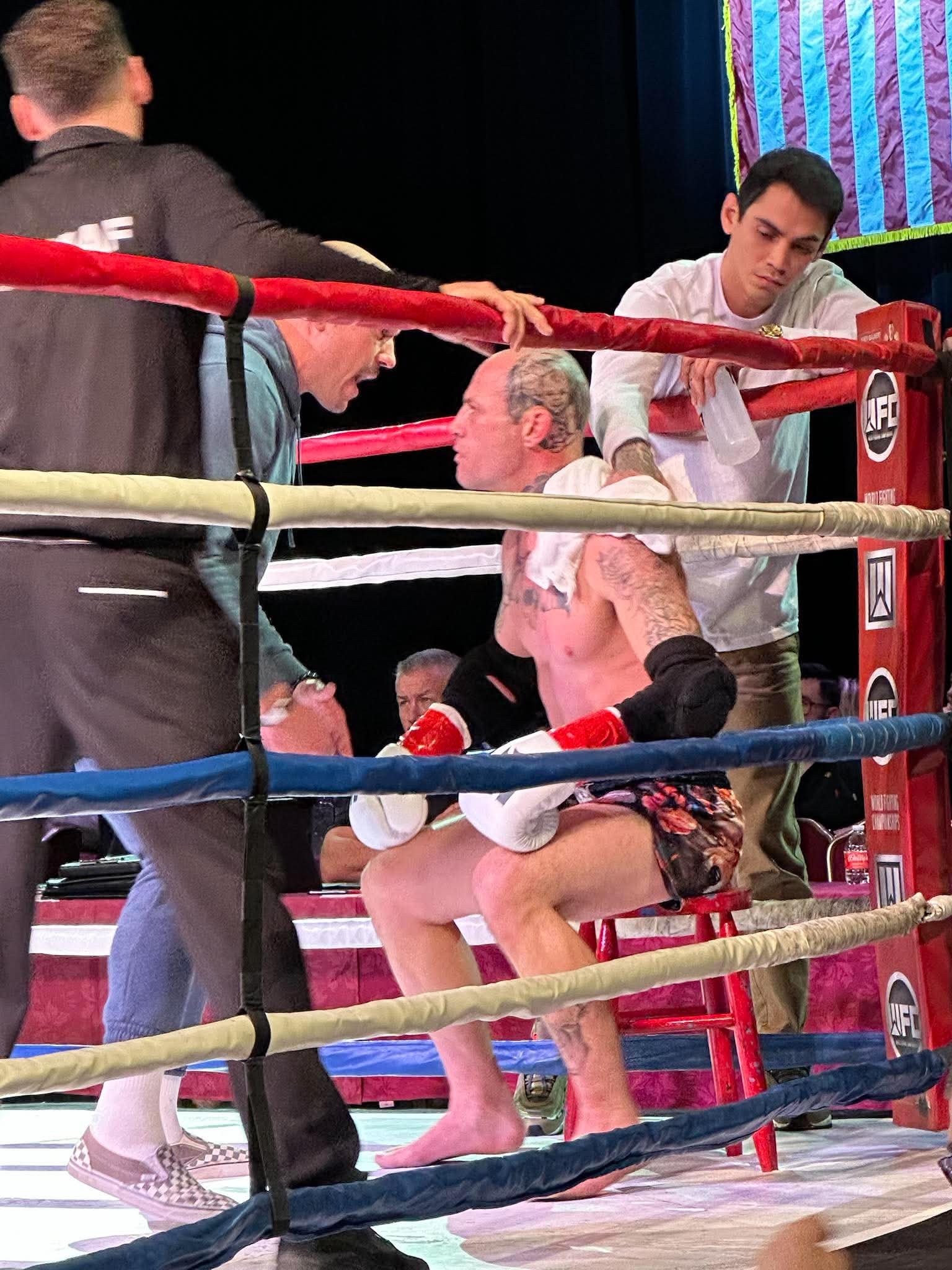 An intense moment in a boxing match where a boxer is seated in his corner with his eyes closed, surrounded by his team inside the boxing ring.