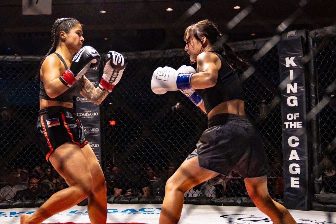 Two female mixed martial artists fighting inside an octagon cage, one throwing a punch at the other.