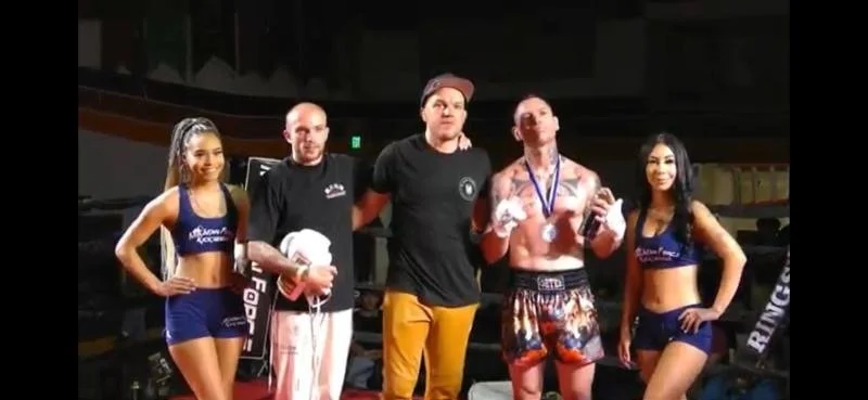 Two female ring girls and two male boxers in the center, posing in a boxing ring after a match.