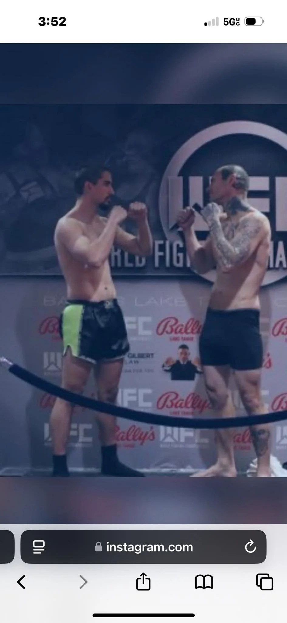 Two shirtless men face each other in a UFC weigh-in, holding microphones in front of a UFC backdrop with promotional logos.