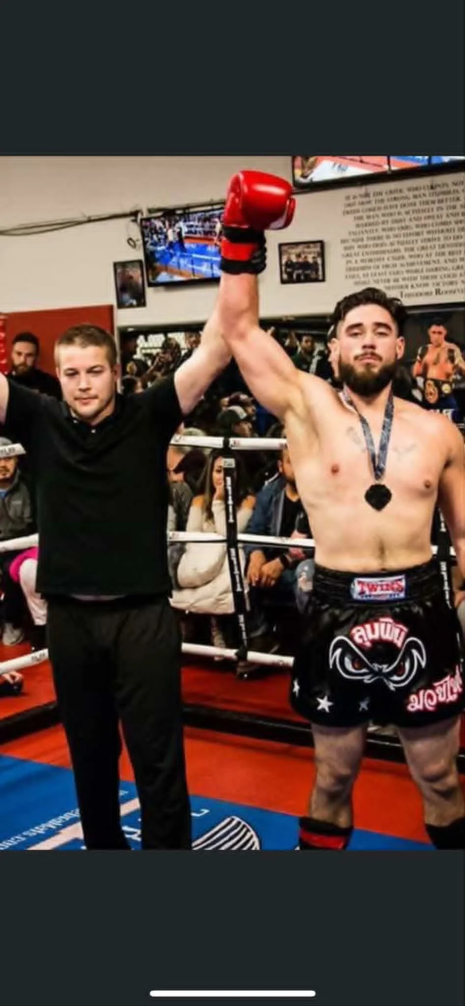 A victorious boxer with a medal, raising his arm in victory, standing in a boxing ring with spectators watching.