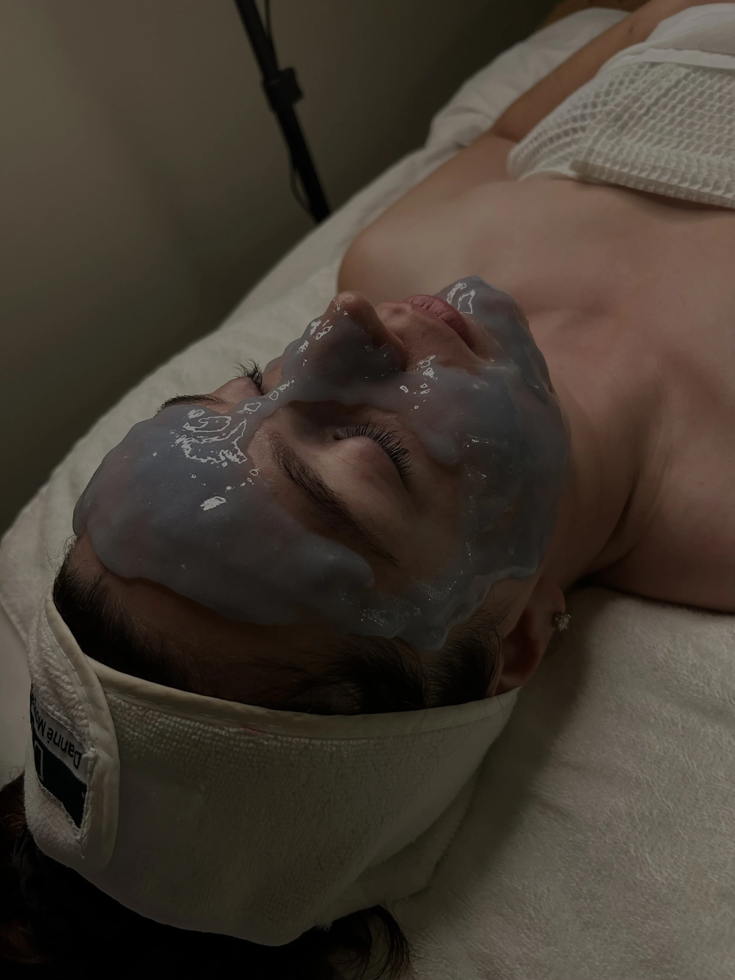 A person lying down with a facial mask applied, resting on a bed with their eyes closed.