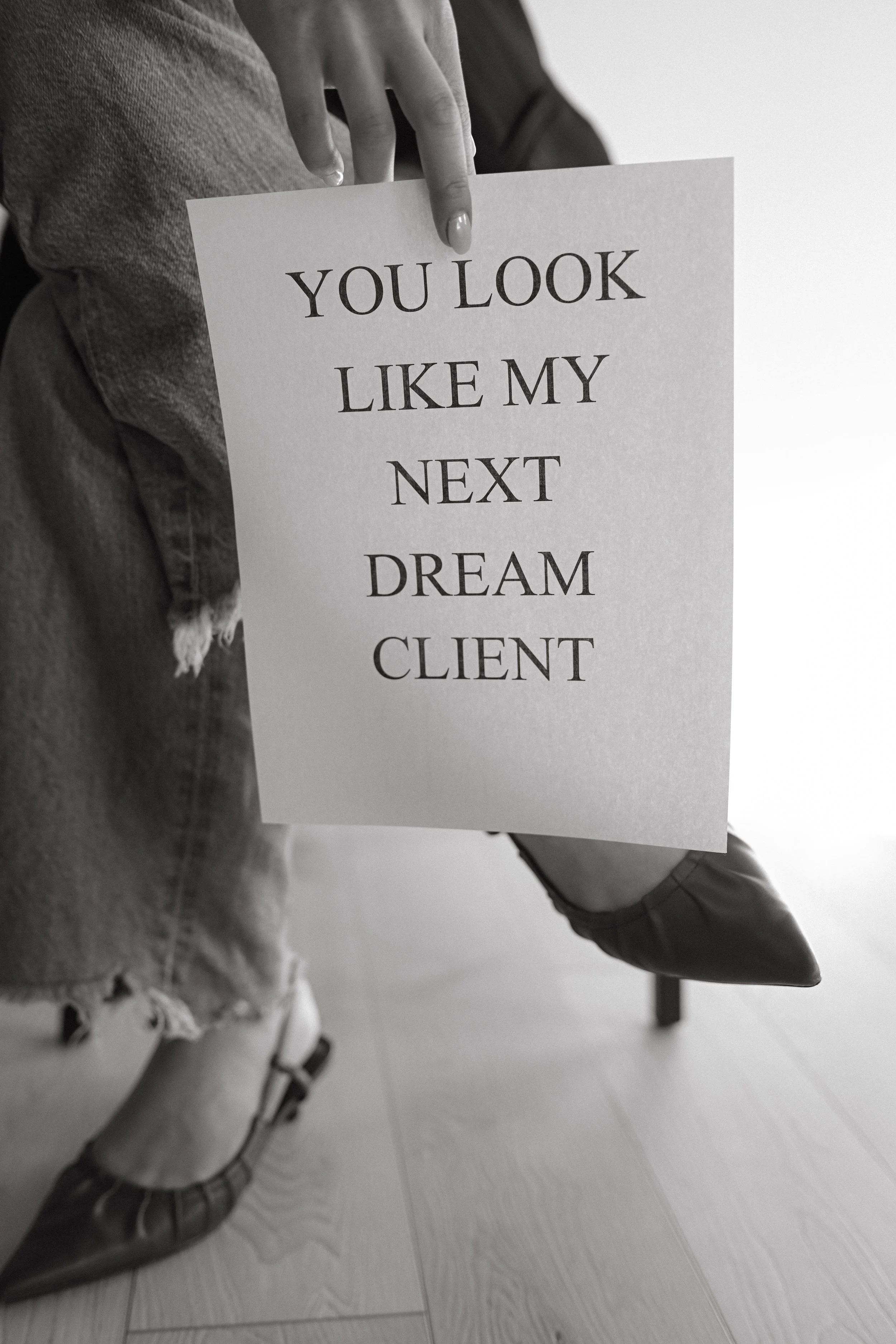 A person wearing boots and torn jeans holding a sign that says "You look like my next dream client."