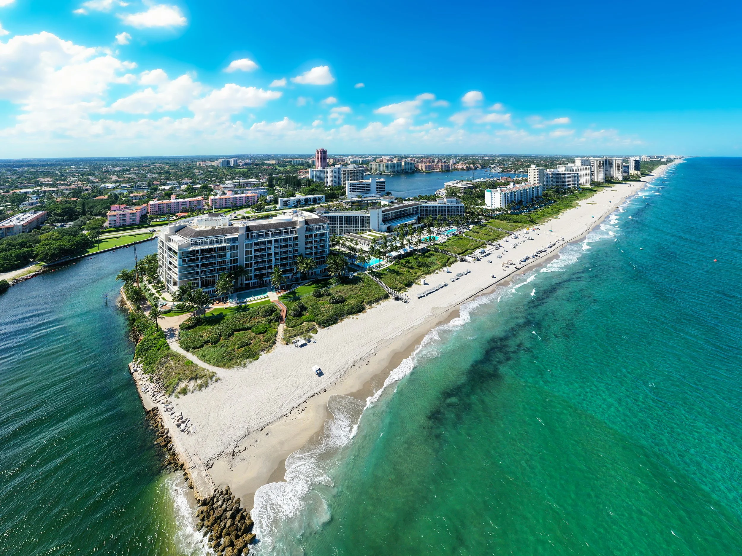 Aerial view of a coastal city with high-rise buildings next to a sandy beach and turquoise ocean waters.