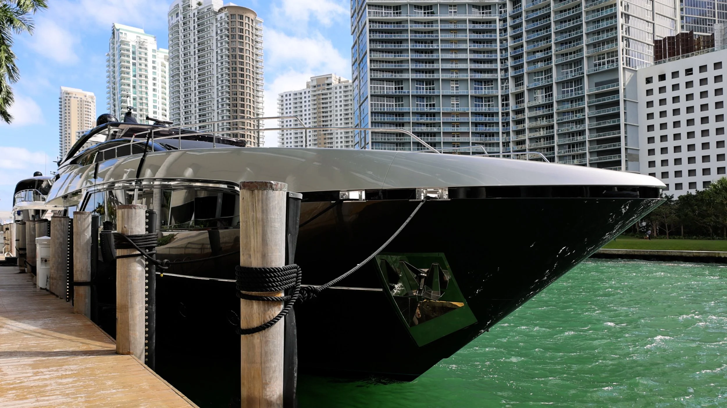 Luxury yacht docked at a marina with high-rise buildings in the background on a sunny day.