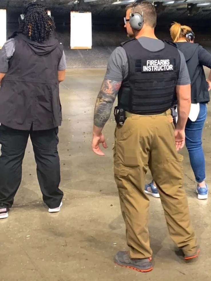 A police officer in tactical gear at a shooting range, wearing a vest labeled 'FIREARMS INSTRUCTOR,' standing with others who are aiming at targets in the background.
