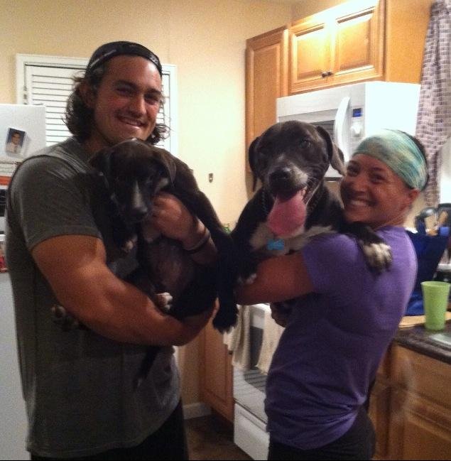 Two people holding black and white puppies in a kitchen with wooden cabinets and a white microwave.