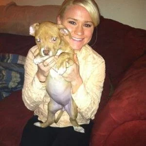 A woman holding a small tan puppy in a living room.