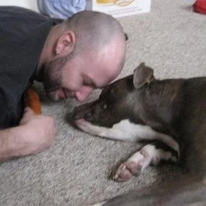 Man lying on carpeted floor with head close to a dog, both touching noses.