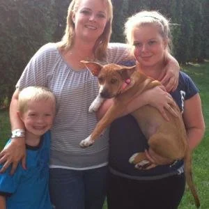 A woman and two children outdoors with a dog, smiling at the camera.